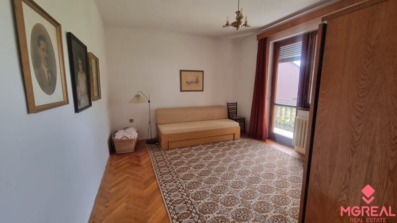 A room in a family house with a sofa, carpet, wood-patterned floor, paintings on the walls.
