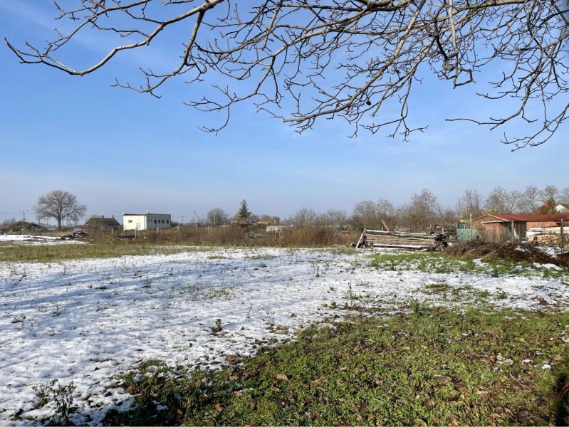 Snow-covered residential plots in the village of Vrakúň, street not specified, with visible houses in the background.