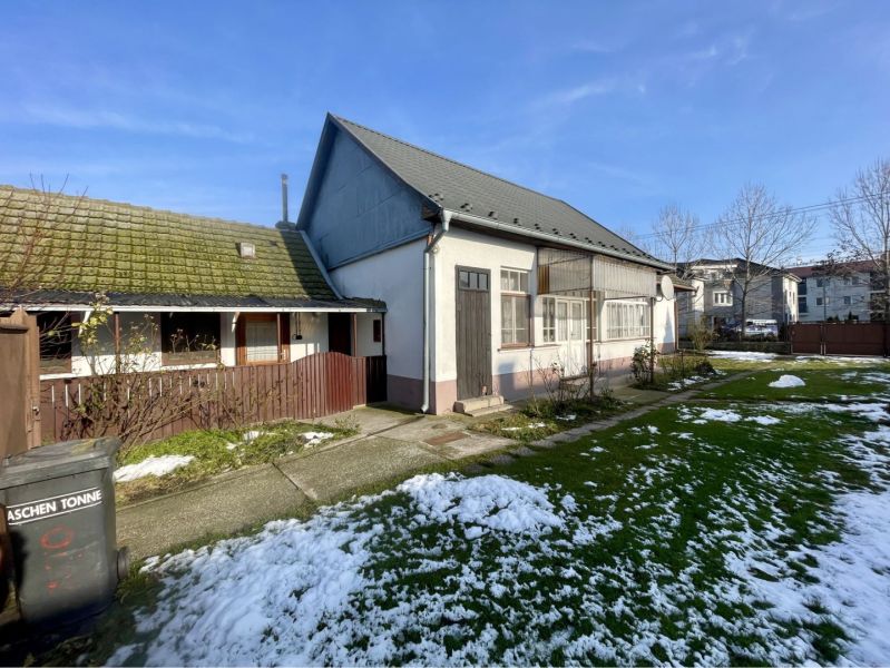 A family house in Vrakúňa with a lawn, remnants of snow, and an adjacent wooden structure.