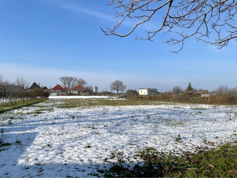 Snow-covered land in Vrakúňa with trees and houses in the background. Plots - residential.