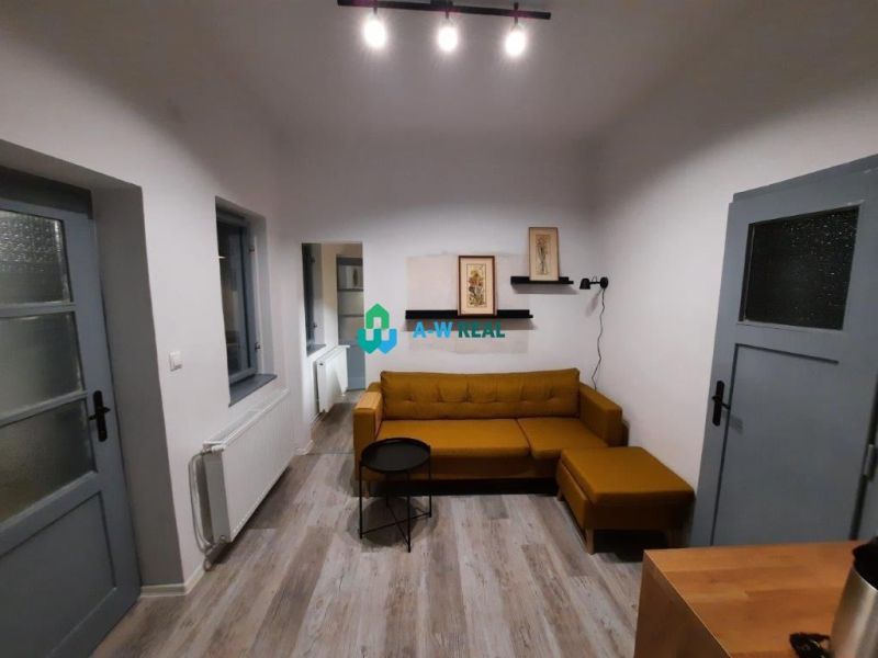 Living room in a family house with a mustard sofa and a wooden-patterned floor.