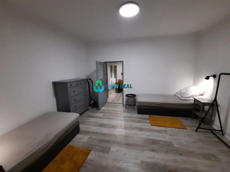 A room in a family house with two beds, gray furniture, and a wooden decor floor.