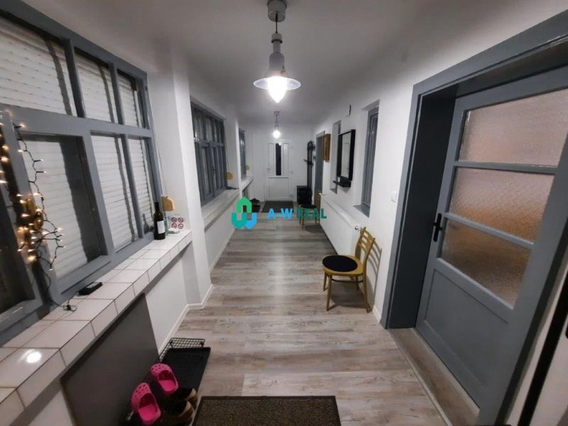 A narrow corridor in a family house with a wooden decor floor, light walls, and windows.