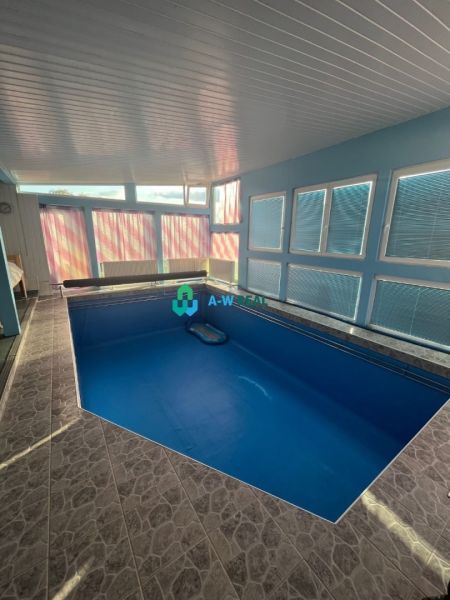 Interior of a family house with a pool and tiles, surrounded by windows letting in light.