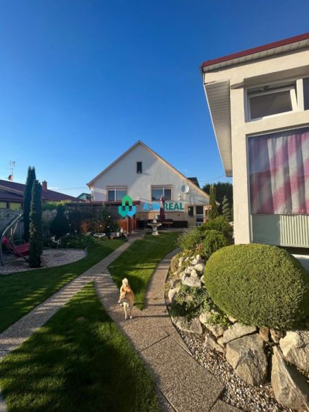 A family house in Orechová Potôň with a well-maintained garden, a walkway, and a dog running around on the lawn.