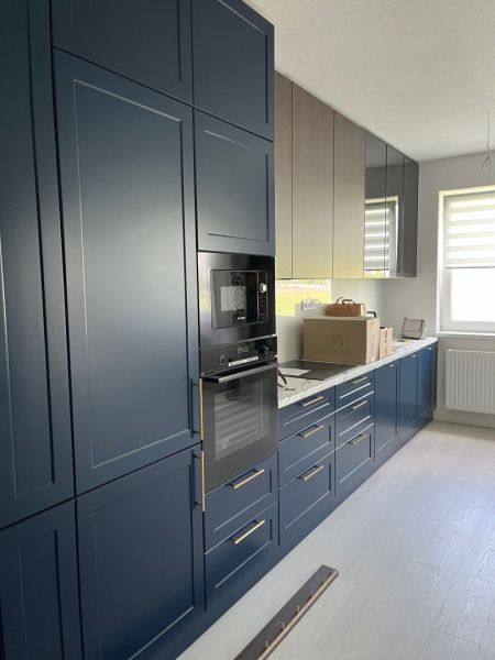 A kitchen in a 3-room apartment with dark blue cabinets and a wooden decor floor.