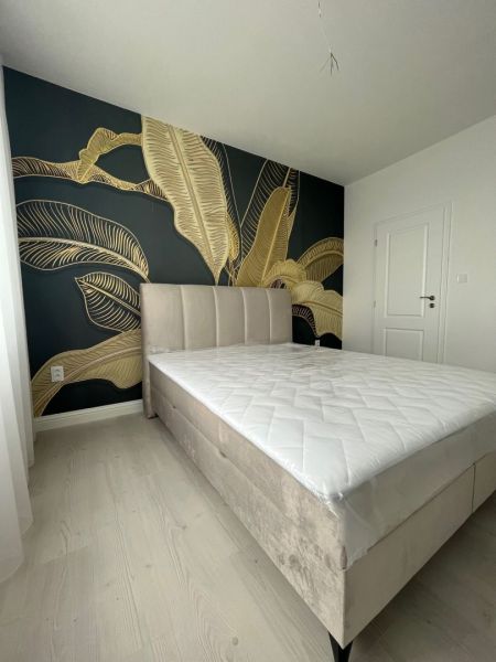 A bedroom in a three-room apartment with a large bed and a bold plant-patterned wallpaper.