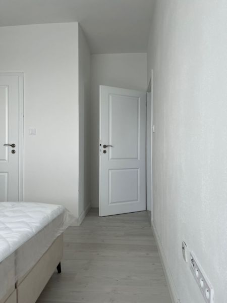 A bedroom with white walls and a wooden decor floor in a three-room apartment.