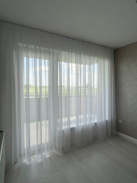 White curtain in a 3-room apartment, floor with wooden decor and light wall.
