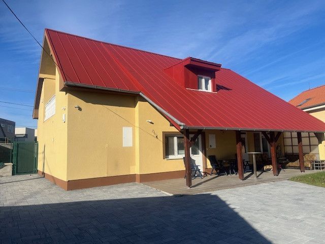 Yellow building with a red roof in Dunajská Streda, paved courtyard and sidewalk.
