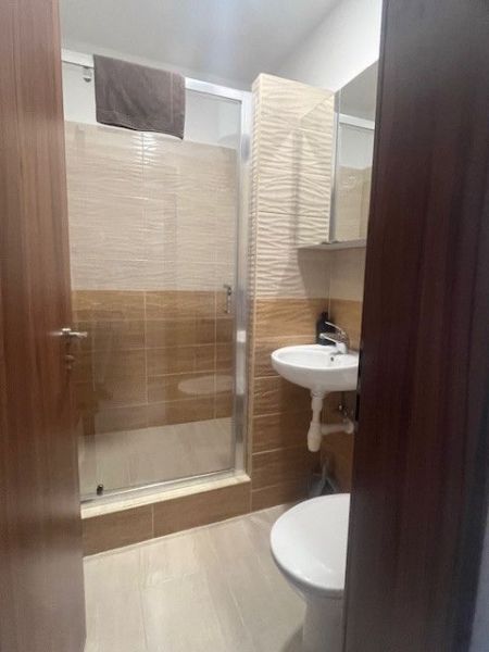 A bathroom in a building with a shower, a sink, and a floor with a wooden decor.