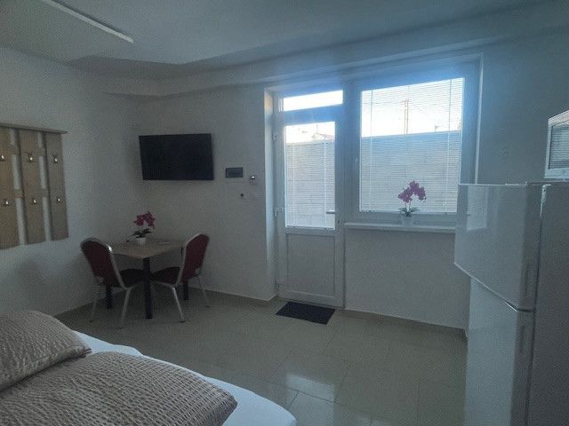 A room with a television, table, chairs, window, and a flower on the windowsill.
