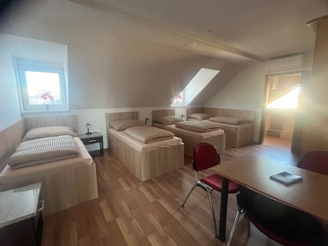 A room with three beds, a wooden floor design, and red chairs by the table.