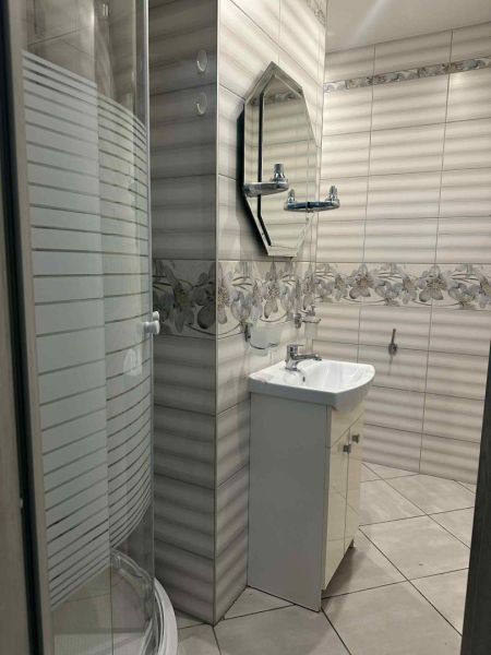 Bathroom with ceramic tiles, a shower corner, and a sink in a studio apartment.
