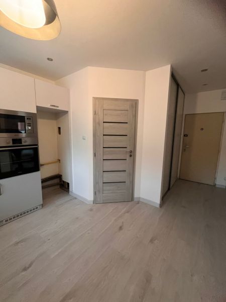 A kitchen in a one-room apartment with a wood-patterned floor and built-in appliances.