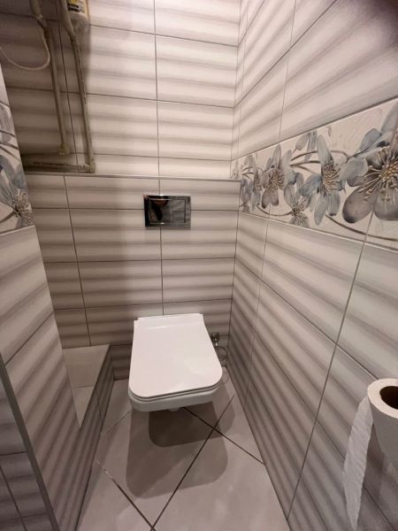 A toilet in a one-room apartment with decorative tiles and a floral motif.