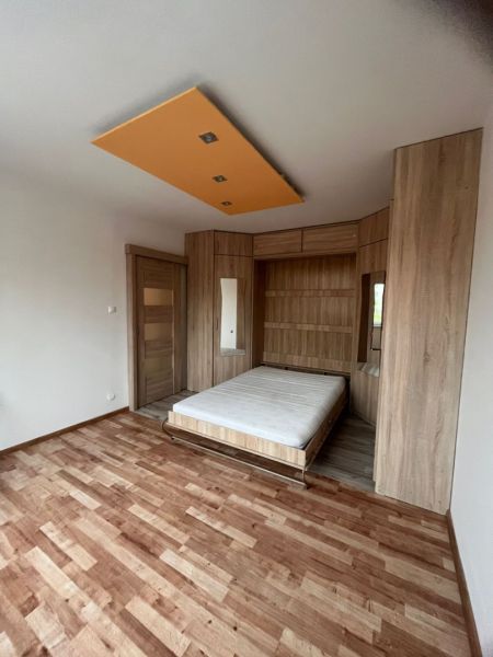 A one-room apartment with a wooden decor floor, a bed, and wooden cabinets.