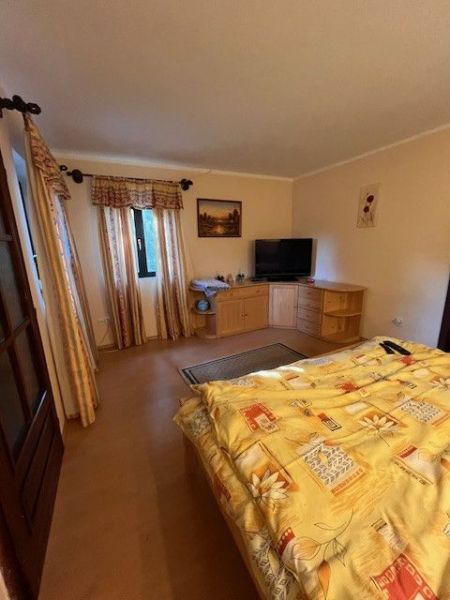 Bedroom in a family house with a bed, dresser, and television, floor with wooden decor.