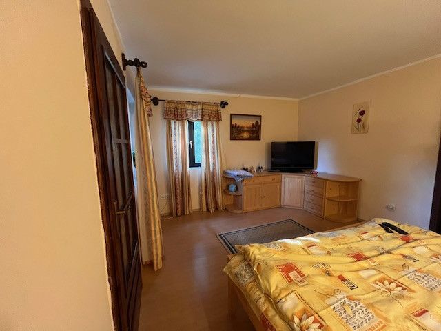 Bedroom in a family house with a television, dresser, and bed, floor with a wooden decor.