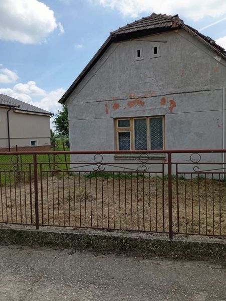 A family house in Ňárad with worn-out plaster and an iron fence, blue sky.