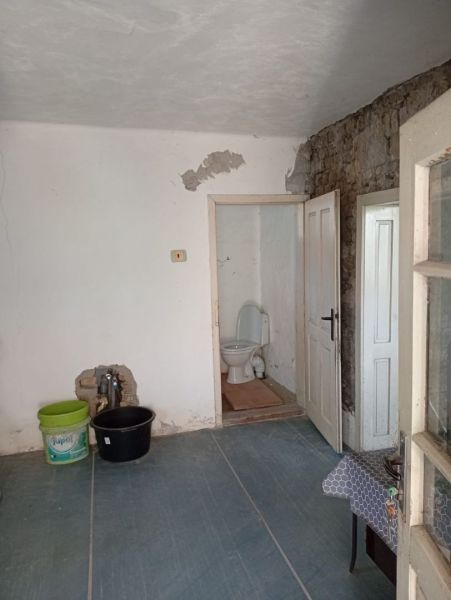 An older room with a toilet, a floor with a wooden decor, walls with peeling plaster.