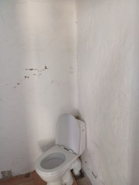 A bathroom in a family house with a white toilet and cracked plaster on the walls.