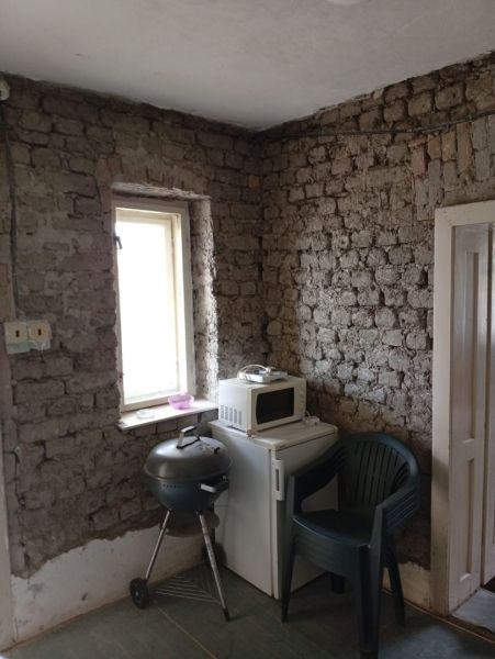 A room with brick walls, a grill, a microwave, and a plastic chair in a family house.
