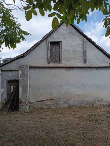 A family house in Ňárad with peeling plaster and a closed attic window, surrounded by greenery.