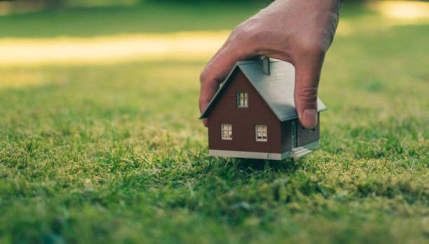 A hand places a small wooden house on the lawn in the gardens of Dunajská Streda.