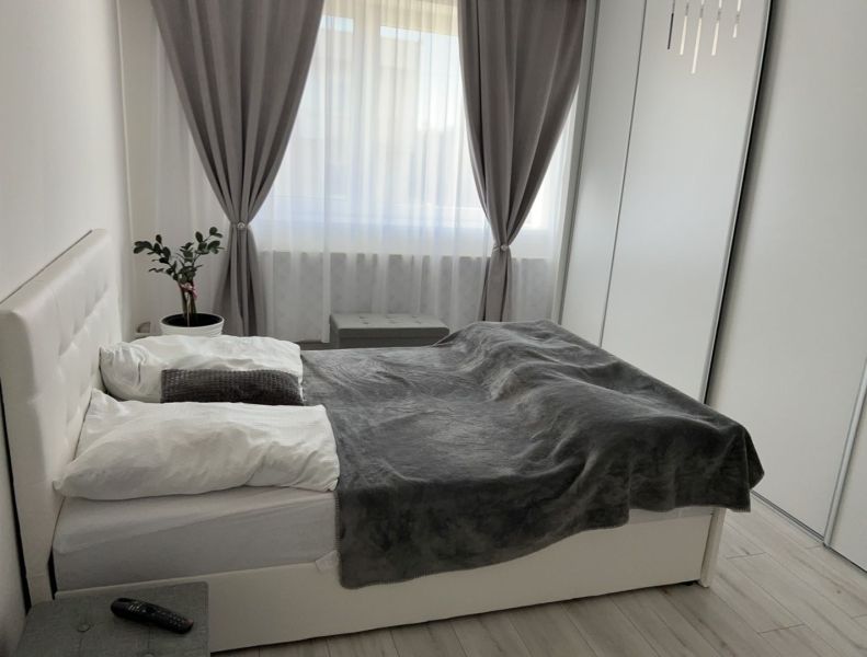 Bedroom with a bed, plant, and curtains, floor with wooden decor in a family house.