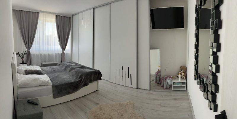 A bedroom in a family house with a wooden decor floor, curtains, a mirror, and a television.