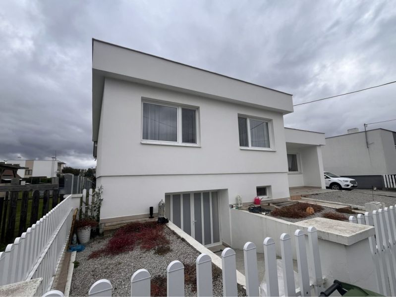A family house in Trstice with a white facade and a white fence under a cloudy sky.