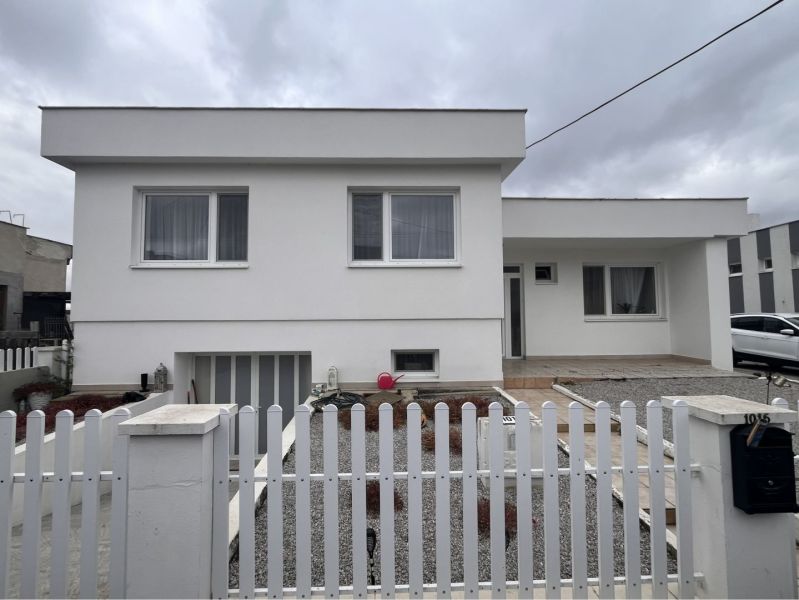 A family house in Trstice with a front garden, a white fence, and a gray-white facade.