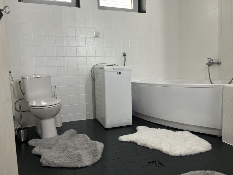 A bathroom in a family house with a bathtub, washing machine, toilet, and fluffy rugs.