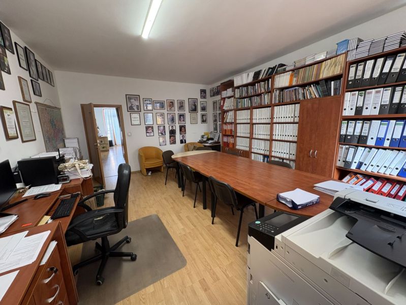 An office with wooden floor decor, a large desk, shelves full of documents, and a computer.