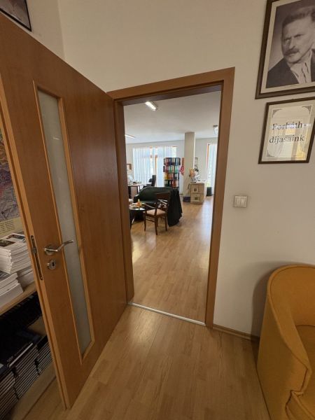 An interior with wood-patterned flooring and open doors leading to an office.