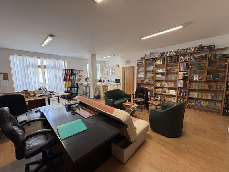 An office with a lot of books, tables, and a wooden decor floor in a 3-room apartment.