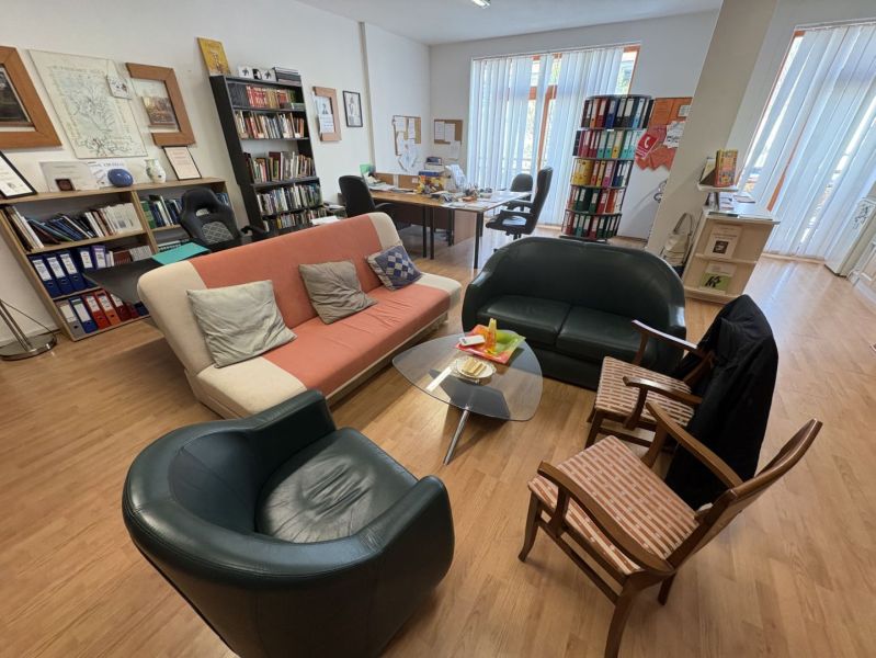 Interior of an office with wood-patterned flooring, sofas, and books.