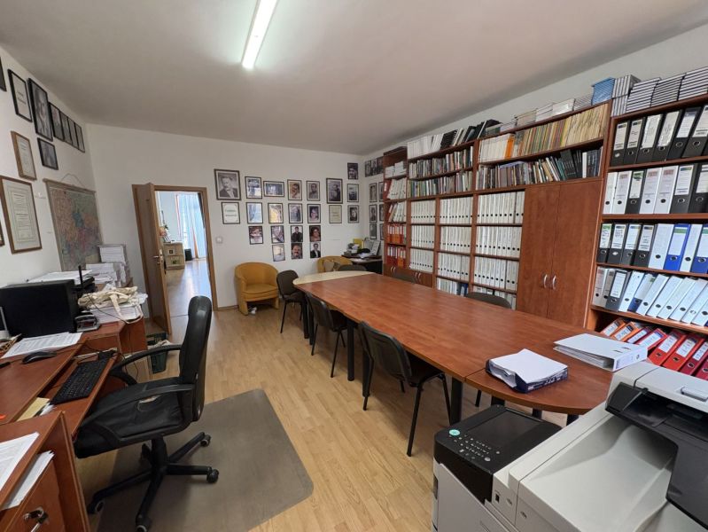 An office with a wood-patterned floor, a desk, chairs, and shelves full of binders.
