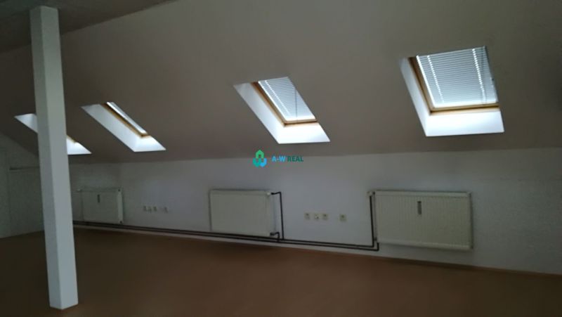 An attic office with radiators, windows, and a wooden decor floor.