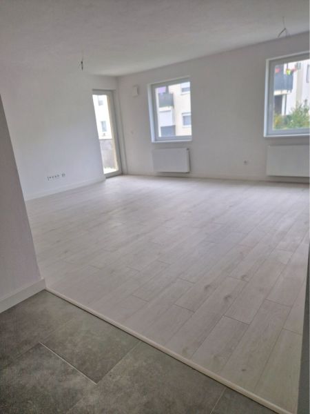 A spacious room in a 3-room apartment with a wooden decor floor and large windows.