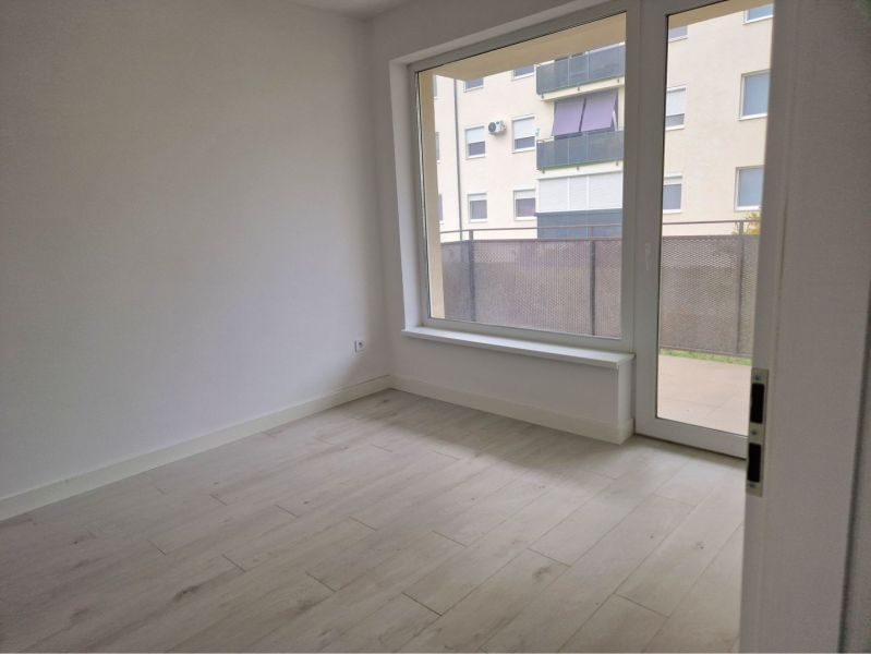 A room with a large window and a wooden decor floor in a 3-room apartment.