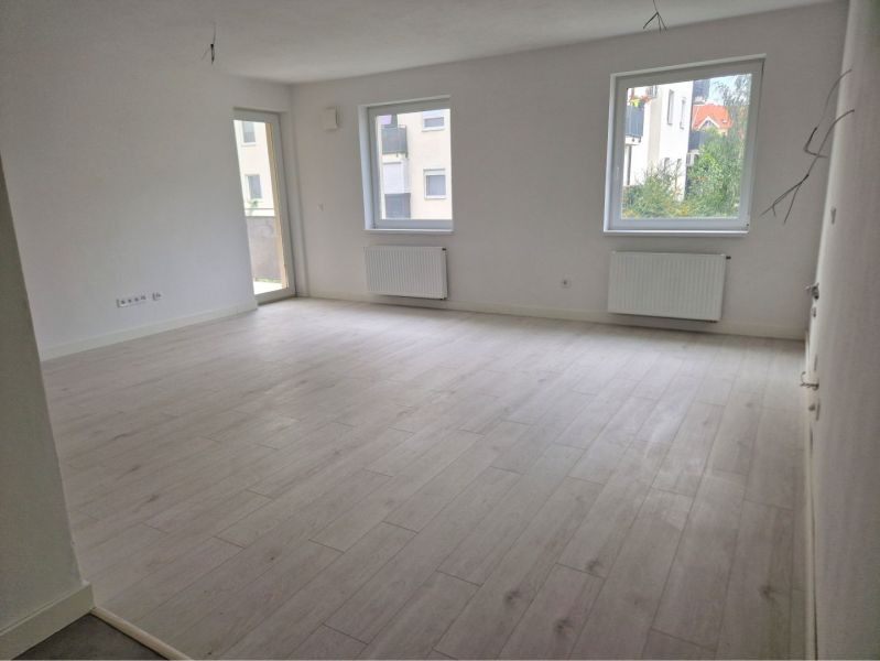 A bright living room with wood-patterned flooring and large windows in a three-room apartment.