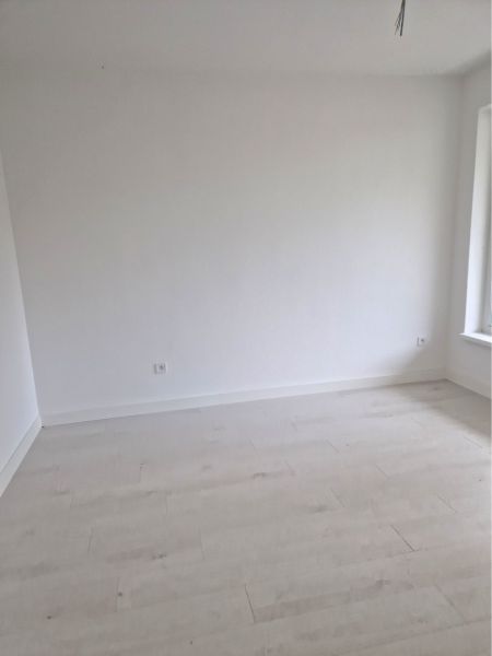 An empty room with white walls and a wooden decor floor in a 3-room apartment.