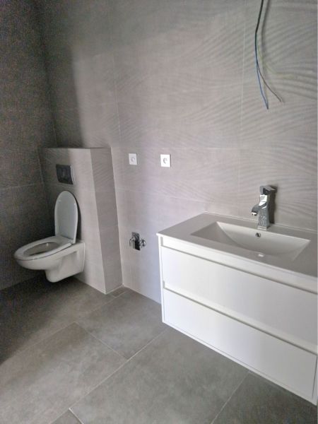 Bathroom in a 3-room apartment with a toilet and a sink, tiles with a neutral design.