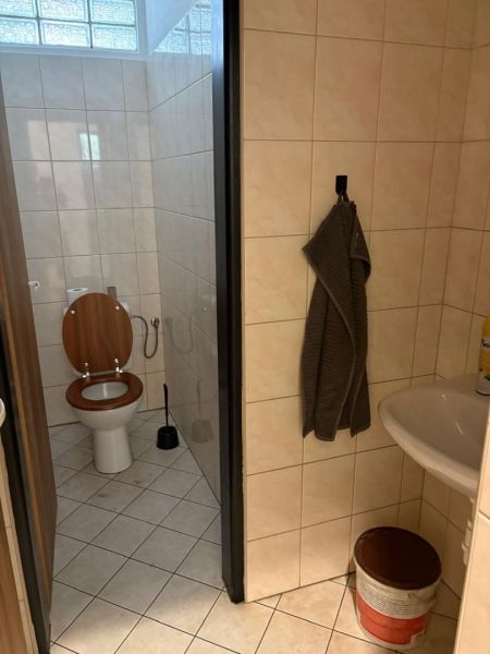Bathroom with toilet, sink, towel, and bucket on the tiles in warehouses and halls.