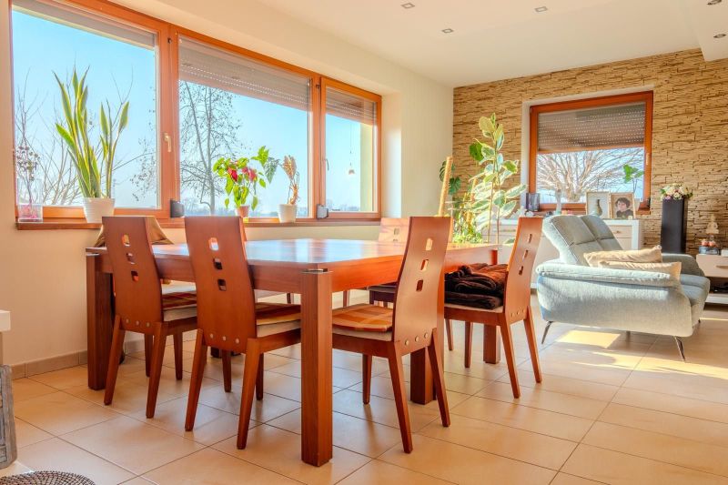 Dining room in a family house with a table, chairs, an armchair, and large windows.