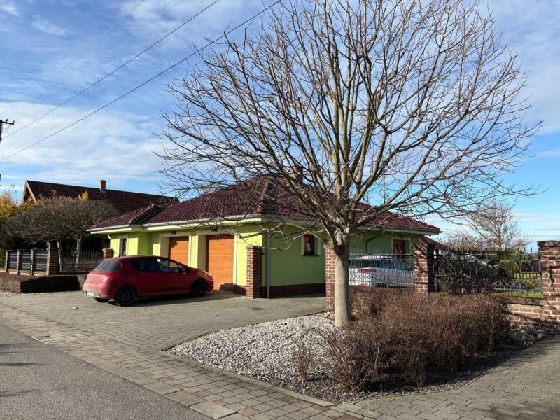 A family house in Dolný Bar with a tree in the foreground and a parked car.