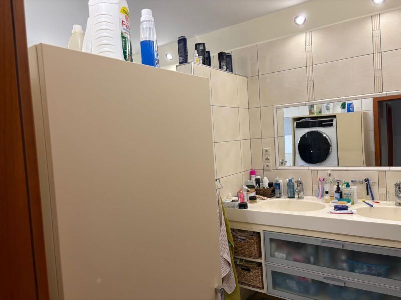 A bathroom in a family house with a double sink and a washing machine in the background.