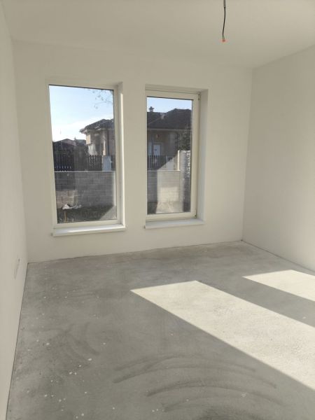 An empty room in a family house with large windows and a concrete floor.